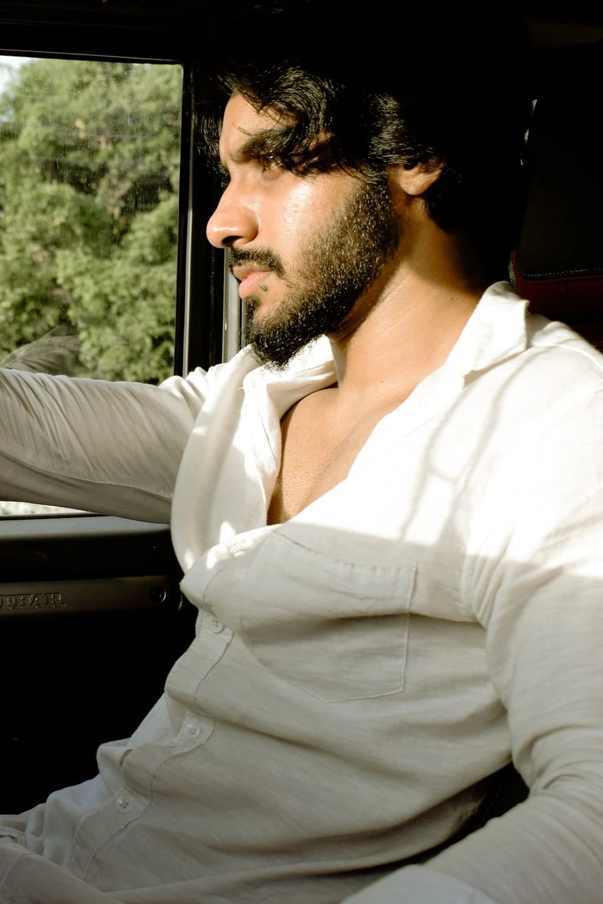 A young man in a white shirt driving a car on a sunny day