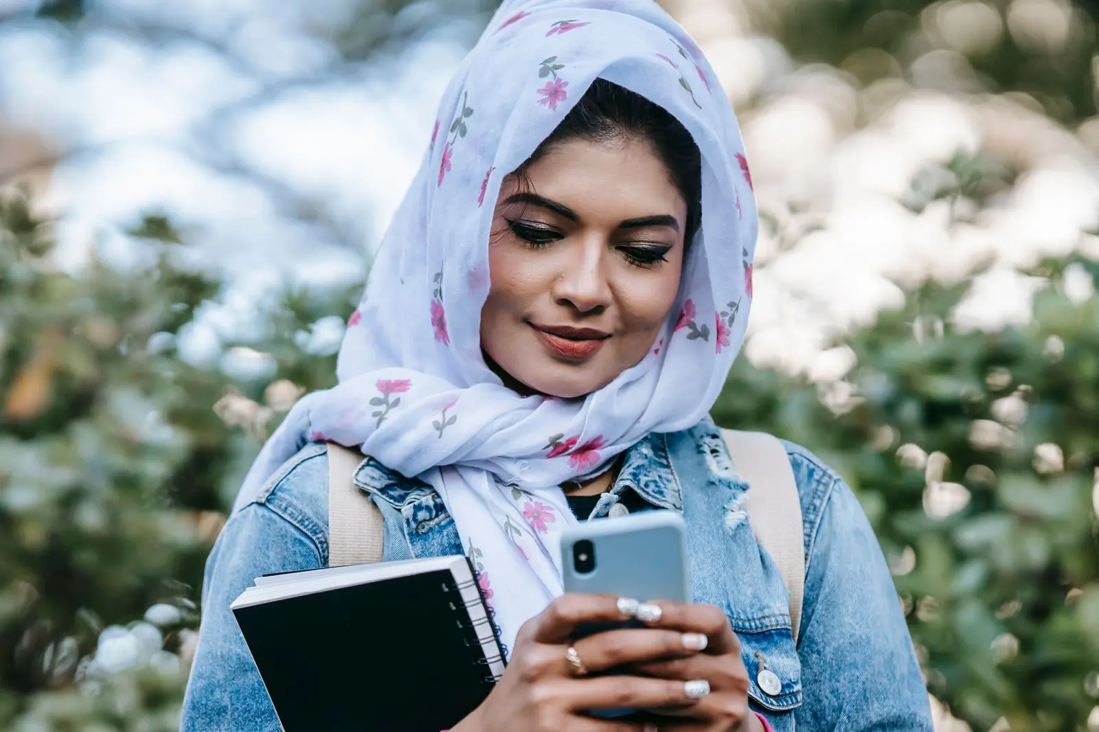A smiling woman in a headscarf using her phone outdoors