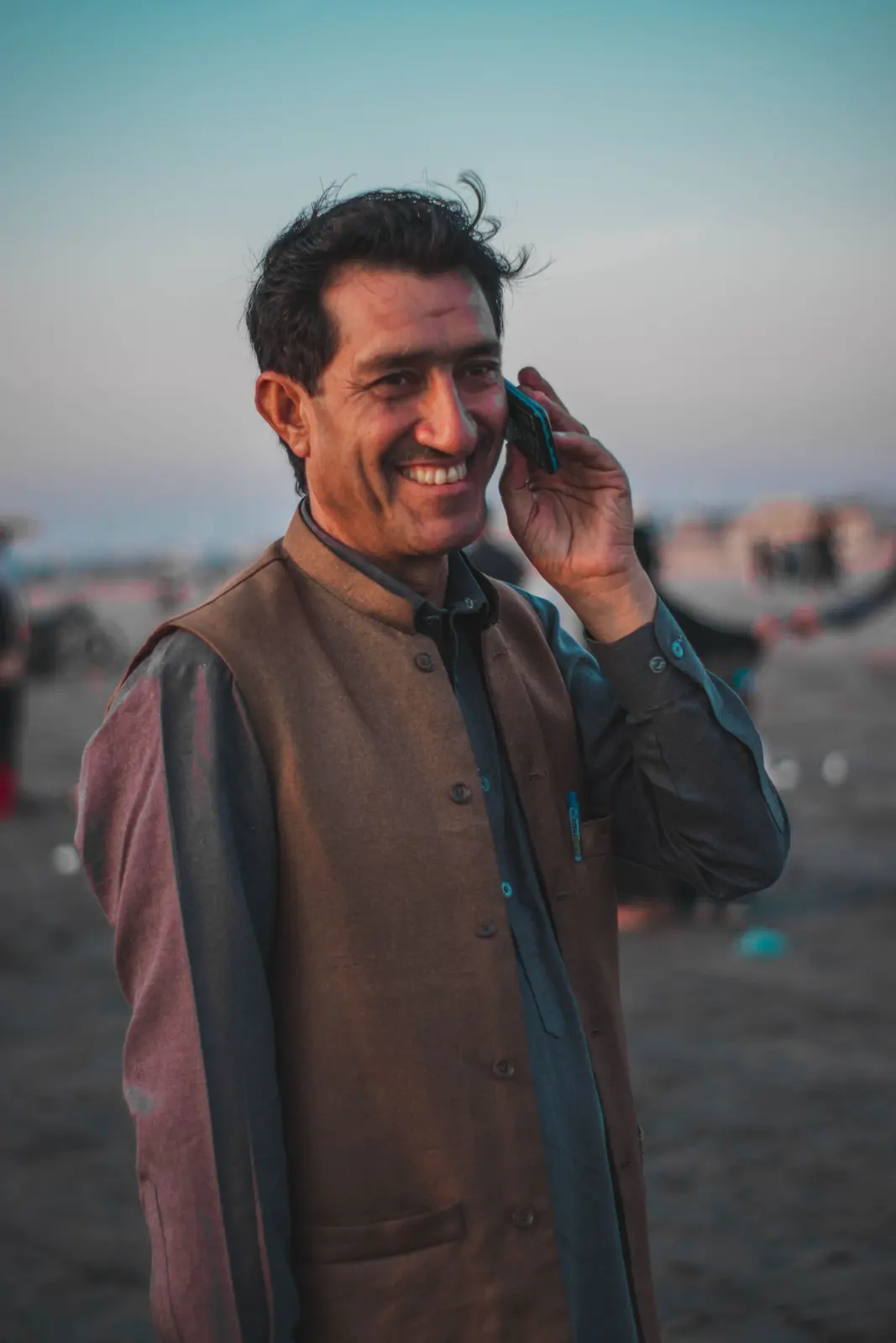 A smiling man in a waistcoat talking on his phone